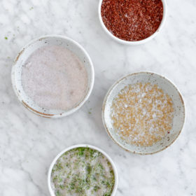 Four dishes with various salt mixtures in them on a grey and white marble surface.