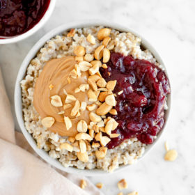 Bowl of steel cut oats topped with peanut butter, jelly, and crushed peanuts.
