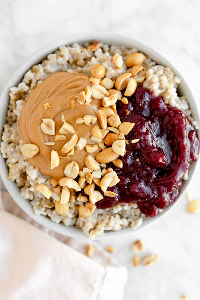 Bowl of steel cut oats topped with peanut butter, jelly, and crushed peanuts.