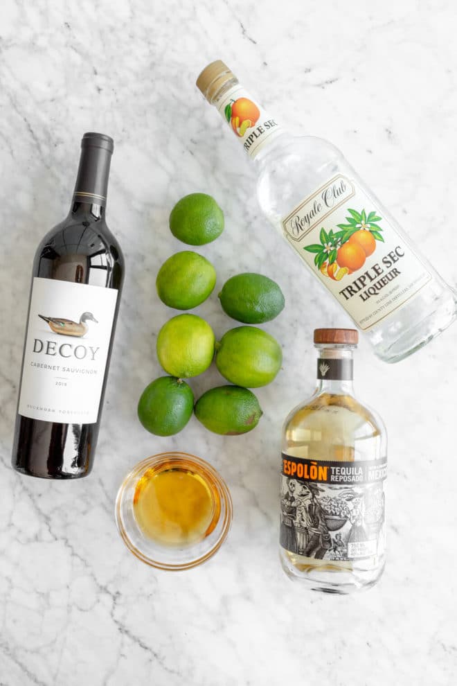 Top down photo of red wine margarita ingredients on a gray and white marble surface.