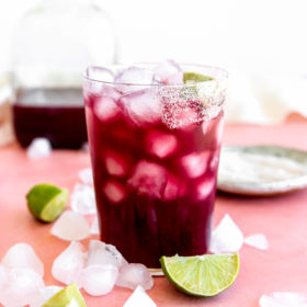 Wine marg on ice in a glass half lined with salt with lime wedges and ice cubes on the table around the glass.