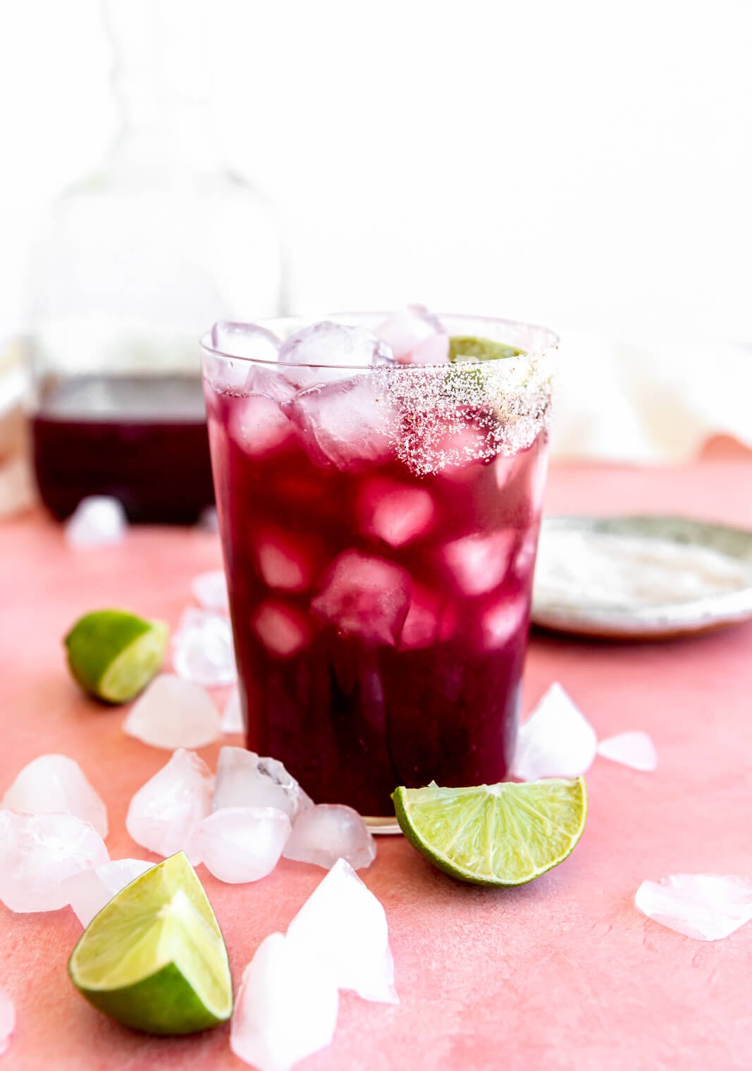 Wine marg on ice in a glass half lined with salt with lime wedges and ice cubes on the table around the glass.