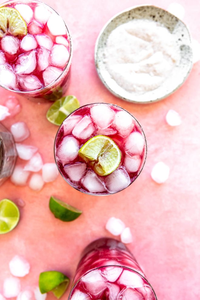 Top down view of 3 wine margaritas in glasses garnished with lime wedges on a blush background with ice cubes and lime wedges and a saucer of salt.