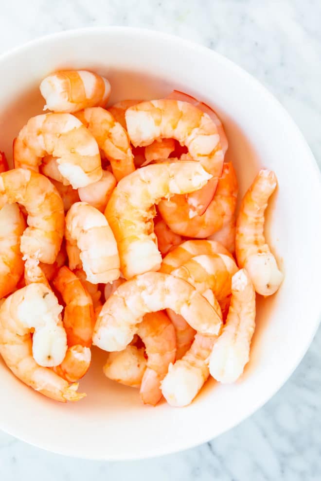 White bowl with cooked, peeled shrimp.