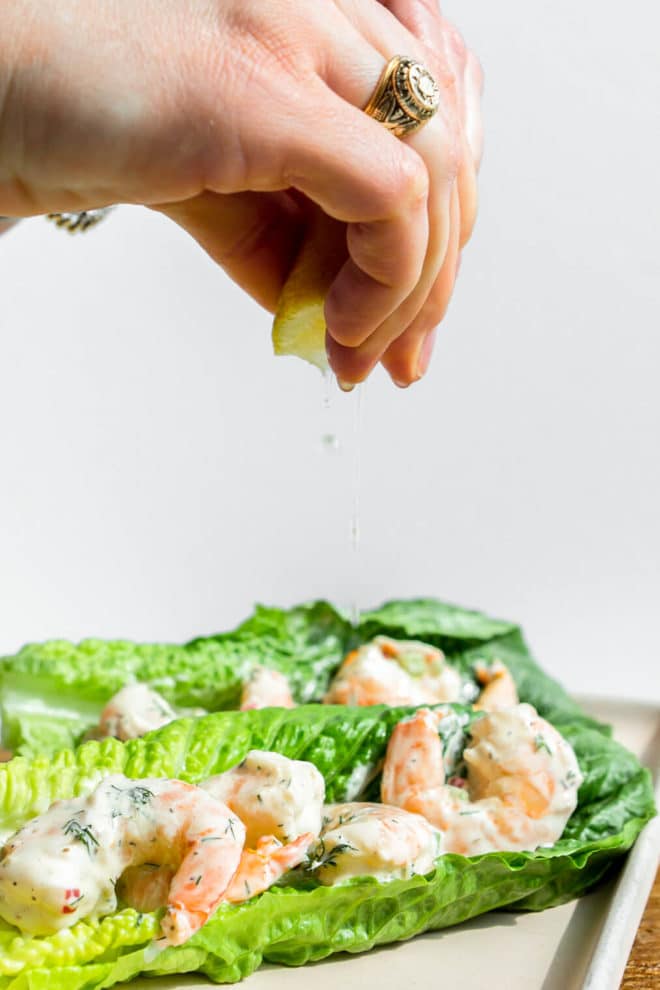 Hand squeezing lemon juice over the top of romaine lettuce leaves topped with shrimp salad.