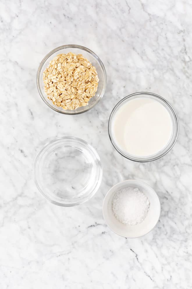 Stovetop oatmeal ingredients in glass bowls on a gray and white marble surface.