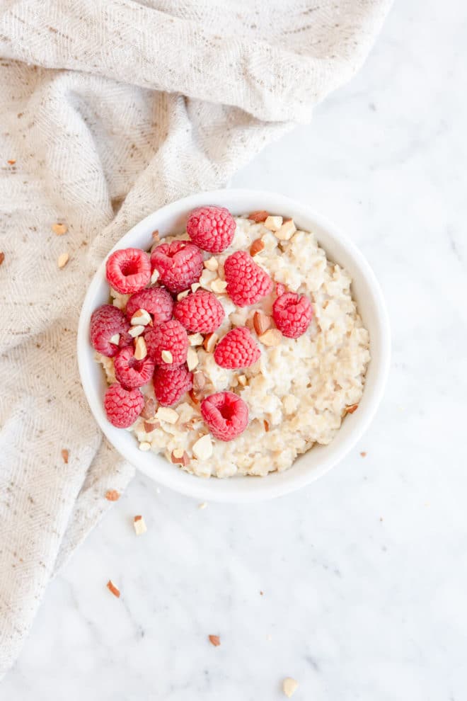 Top down view of white bowl with oatmeal topped with raspberries and chopped almonds. 