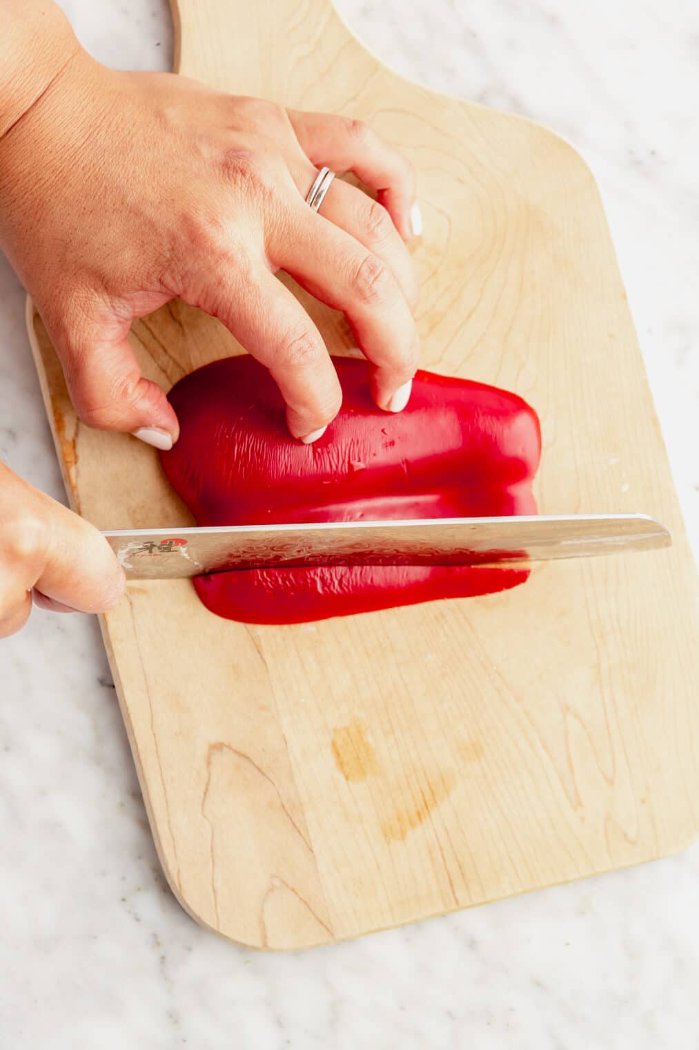 Hand using butcher knife to slice bell pepper.
