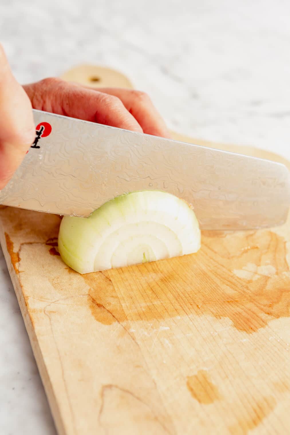 Hand using butcher knife to slice onion.