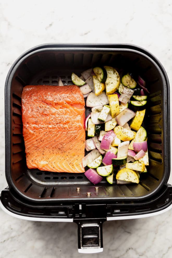 Salmon filet and vegetables side by side in an air fryer basket.