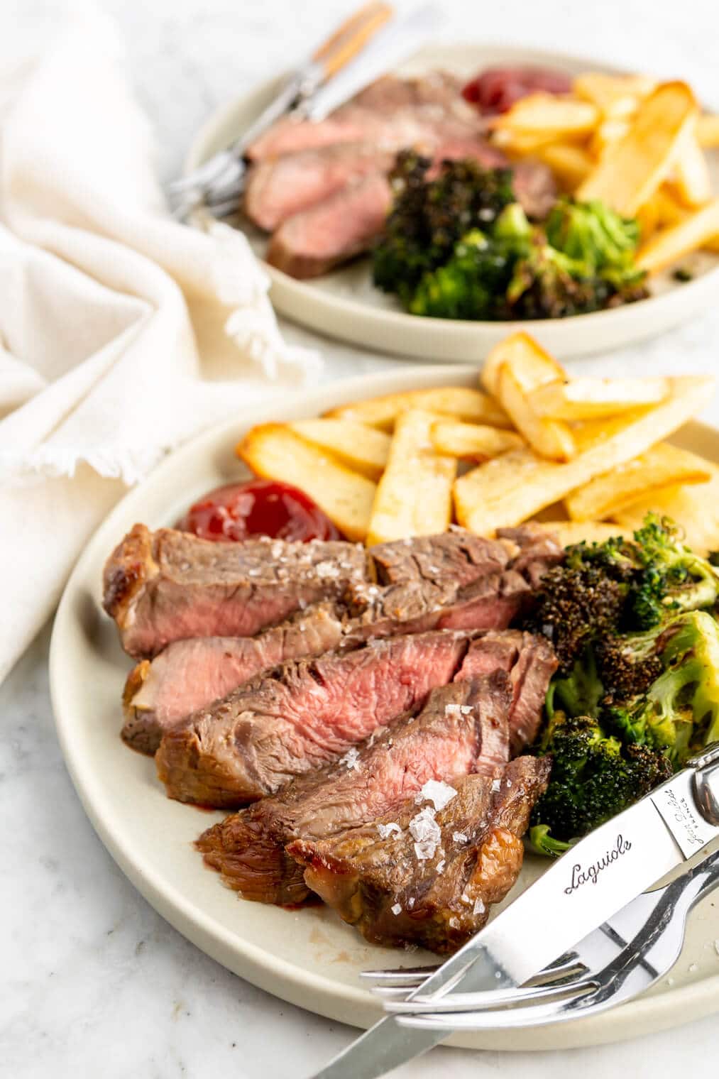 Two air fryer steak dinners plated with broccoli and steak fries.