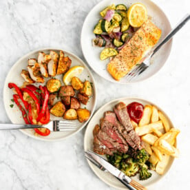 Top down view of three plated air fryer dinners on a gray and white marble surface.