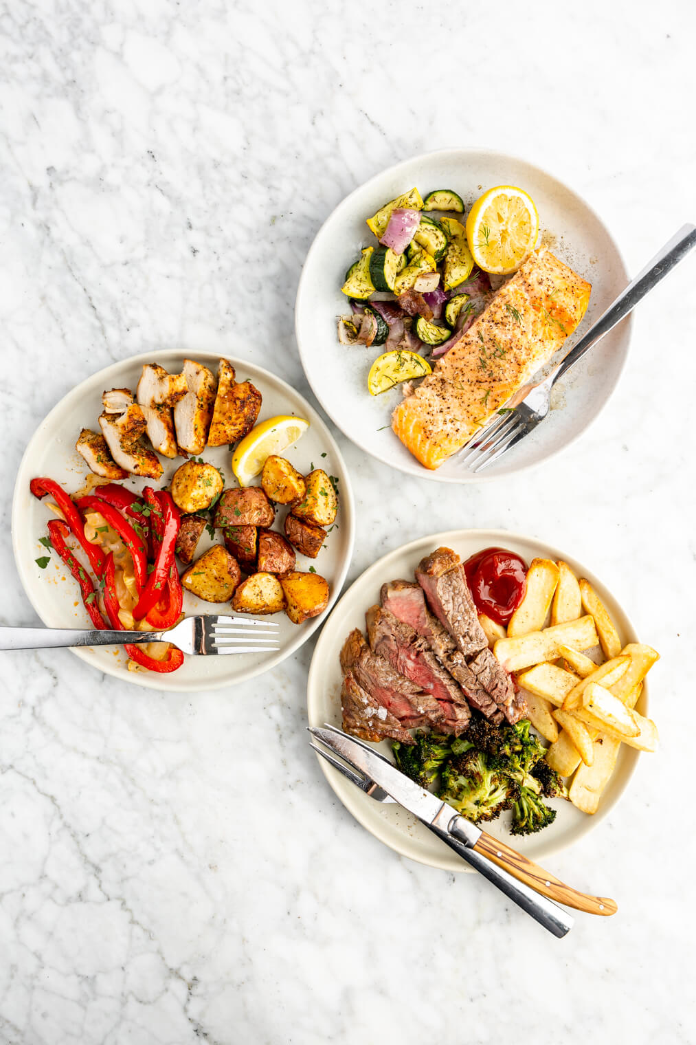 Top down view of three plated air fryer dinners on a gray and white marble surface.