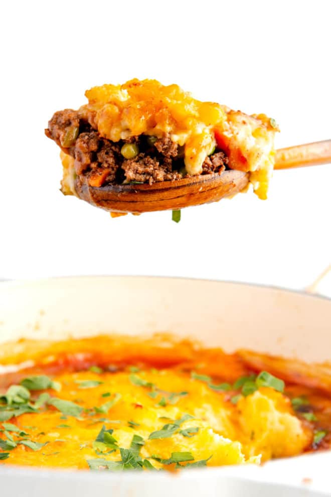 Spoonful of cottage pie held above cottage pie in a casserole dish.