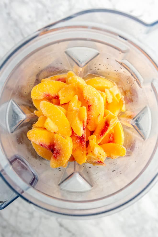 Frozen peach margarita ingredients in a blender pitcher.