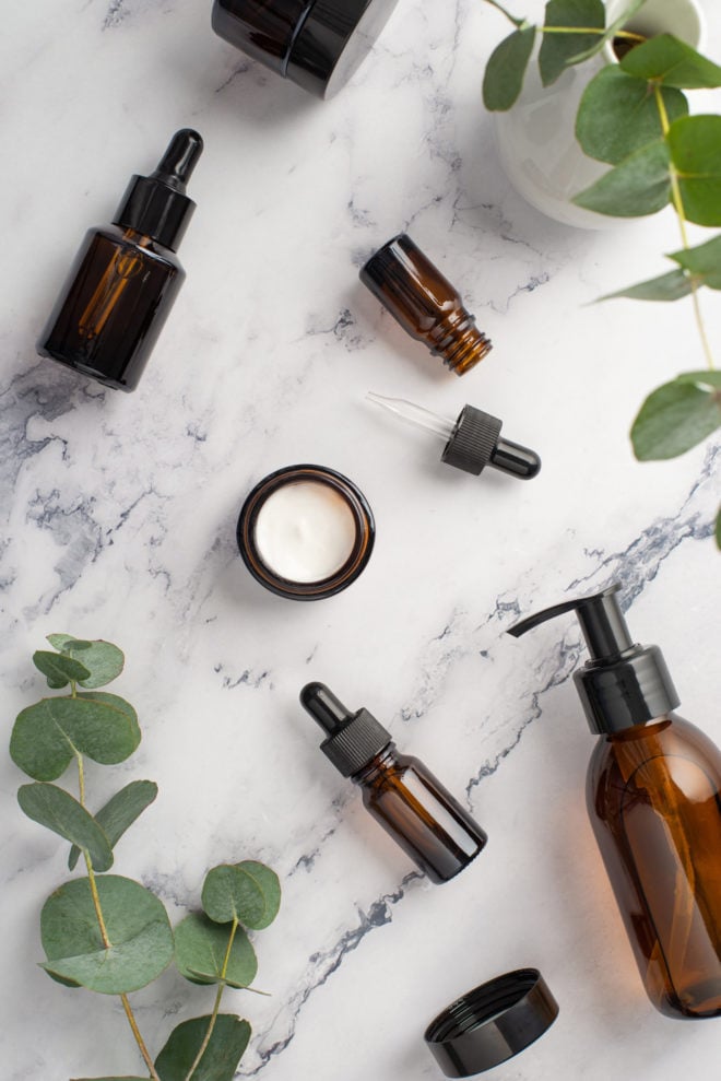 Top view vertical photo of glass bottles with natural cosmetics jar with cream and vase with eucalyptus on white marble background