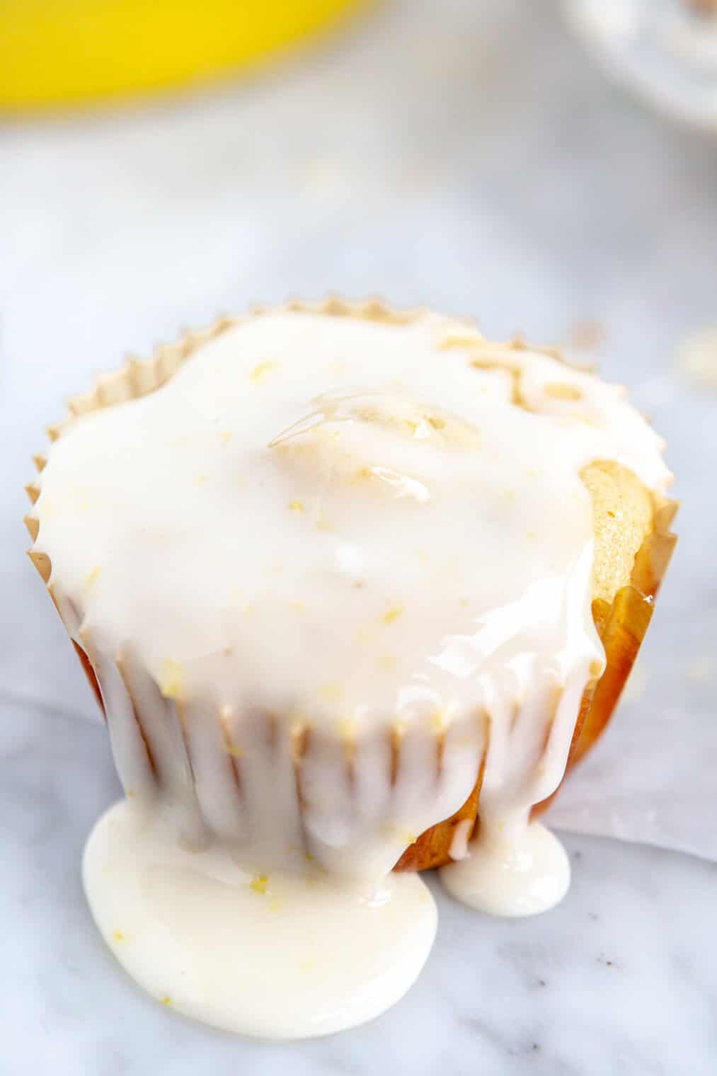 Lemon pistacho muffin topped with glaze on a grey and white marble surface.