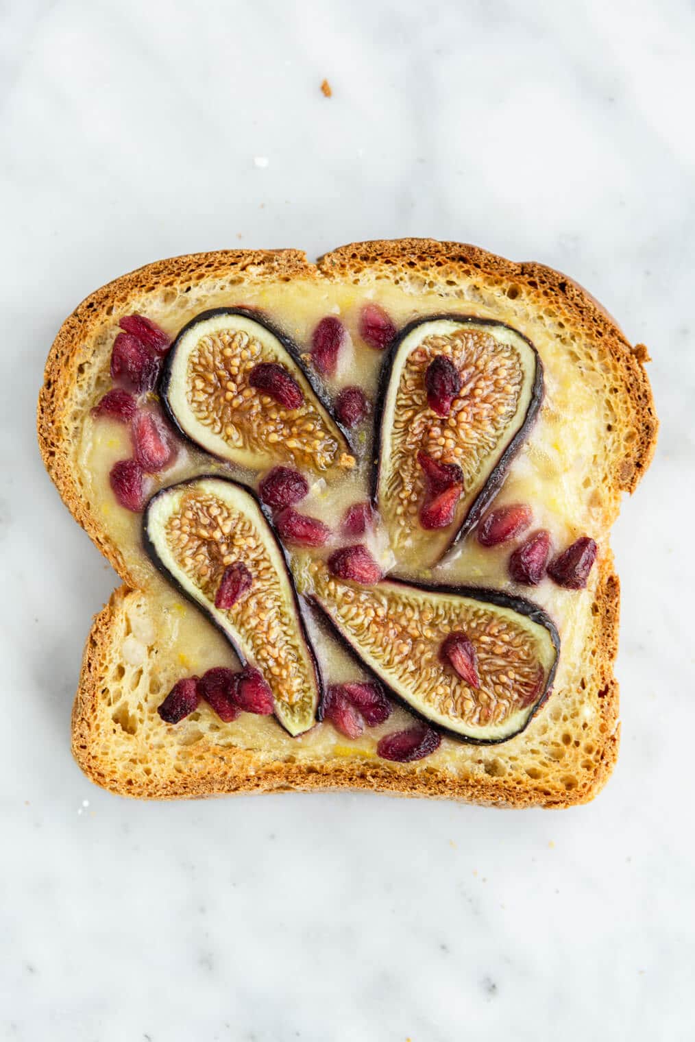 Pomegranate and fig yogurt toast on a grey and white marble background.