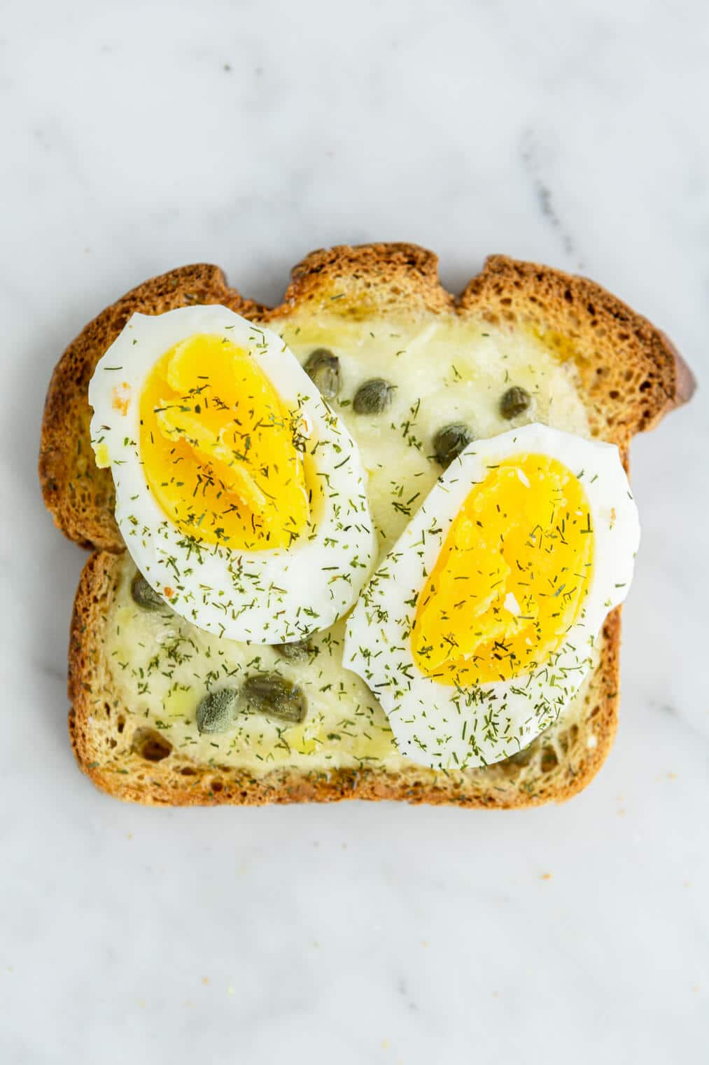 Egg, caper, and dill yogurt toast on a grey and white marble surface.