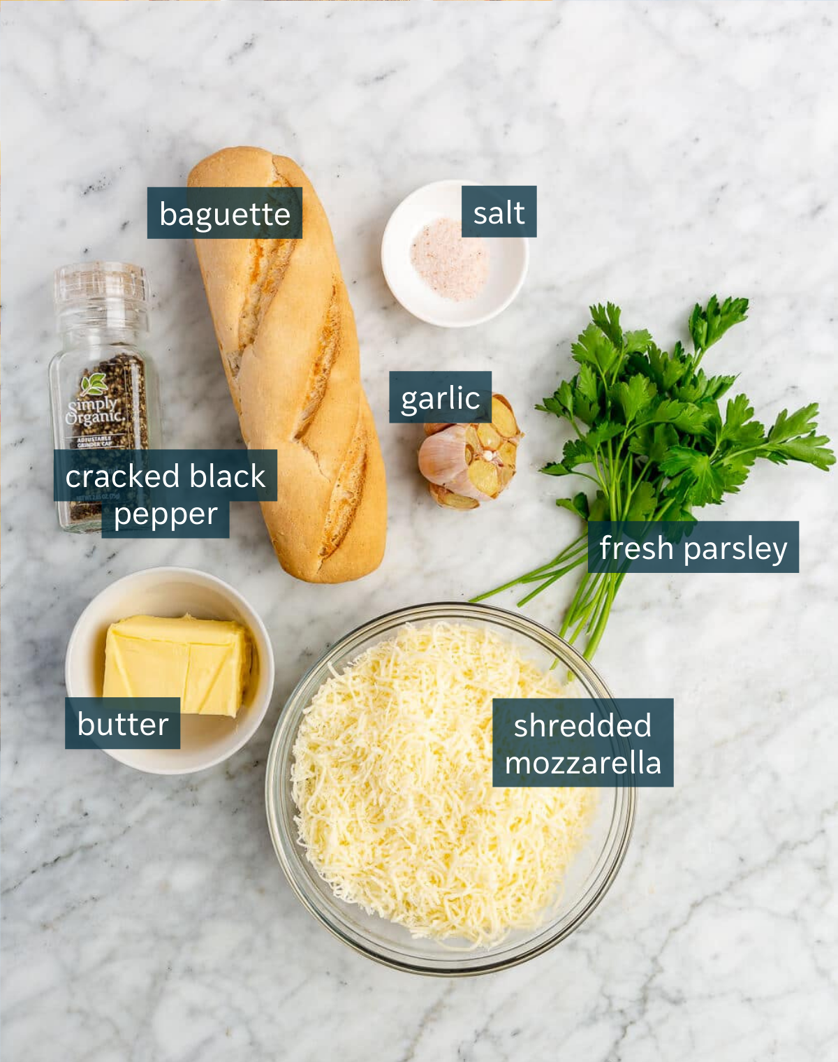Ingredients used to make cheesy garlic bread sit on a marble counter.