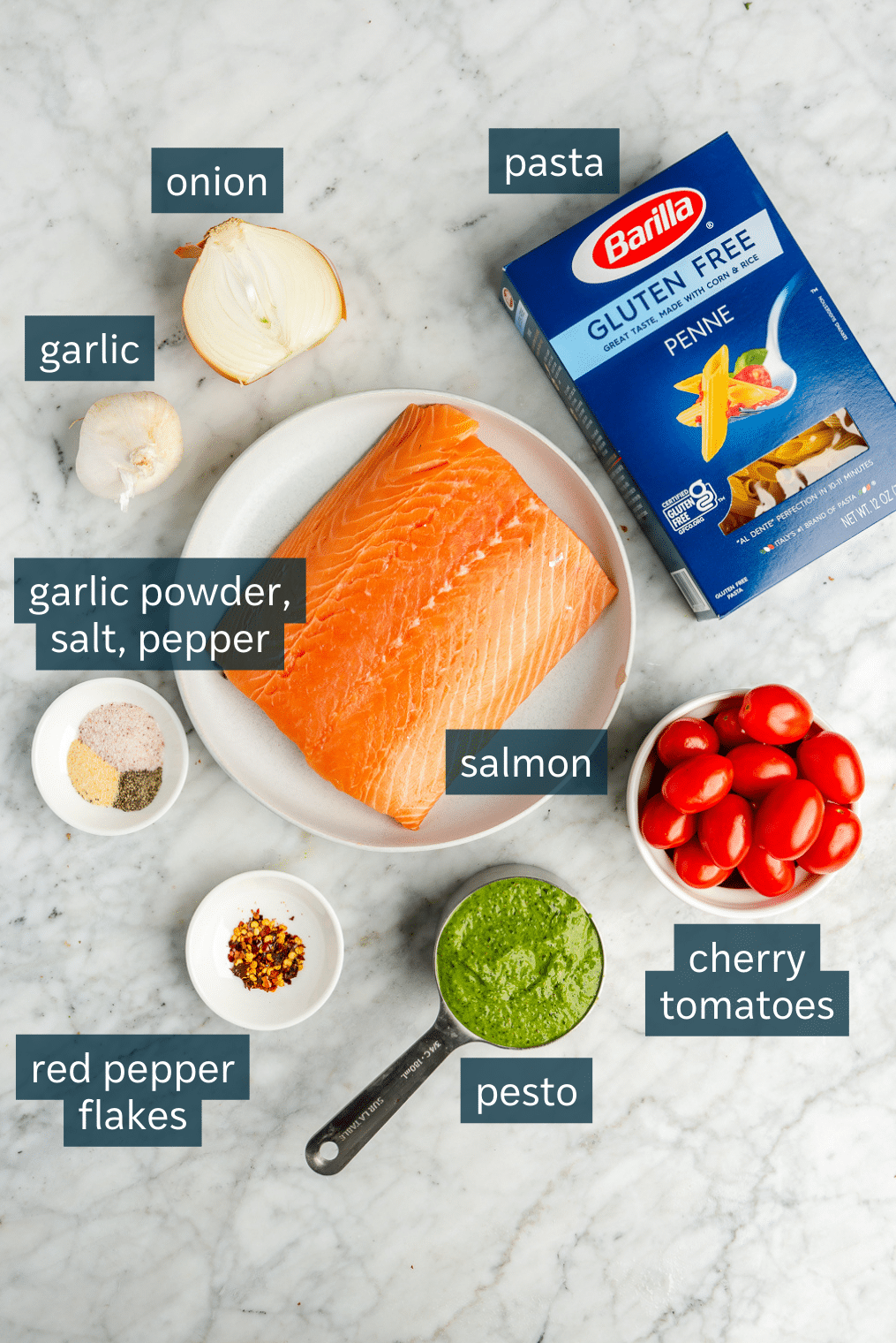 All of the ingredients for salmon pesto pasta on a marble surface.