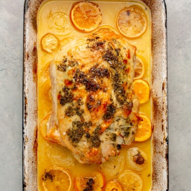 Fully cooked turkey breast is shown surrounded by the, now browned, slices of orange, lemon, and onion. It all sits in the baking pan it was baked in.