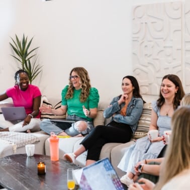Seven women sitting on couches laughing and talking.