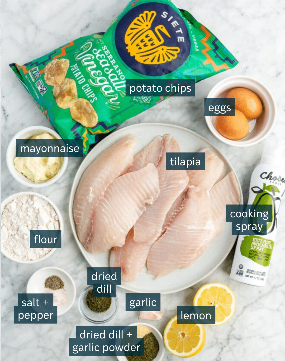 Ingredients for potato chip crusted tilapia with garlic aioli sit in a variety of bowls on a marble countertop.
