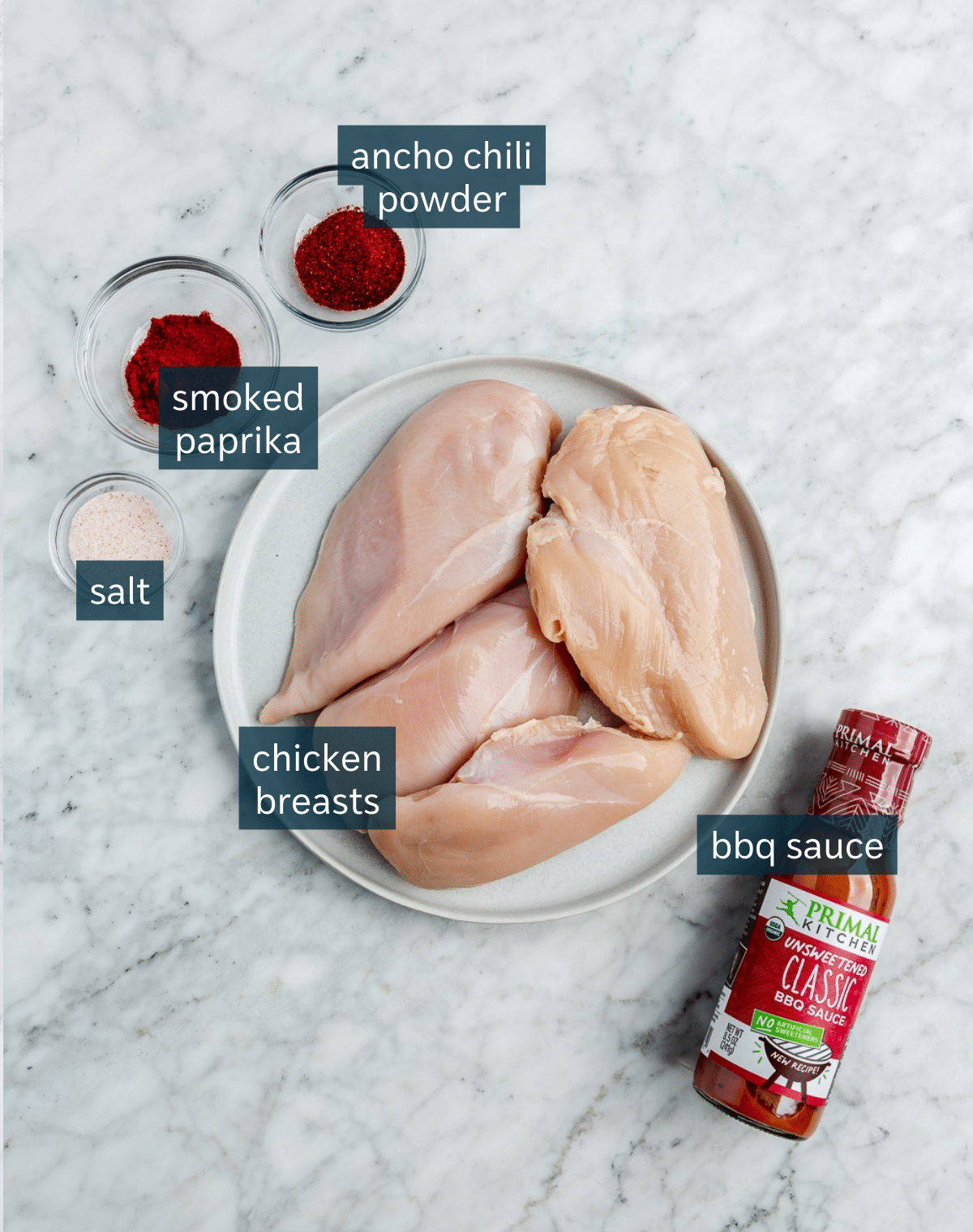 Ingredients for baked bbq chicken breasts sit in a variety of bowls on a marble countertop.