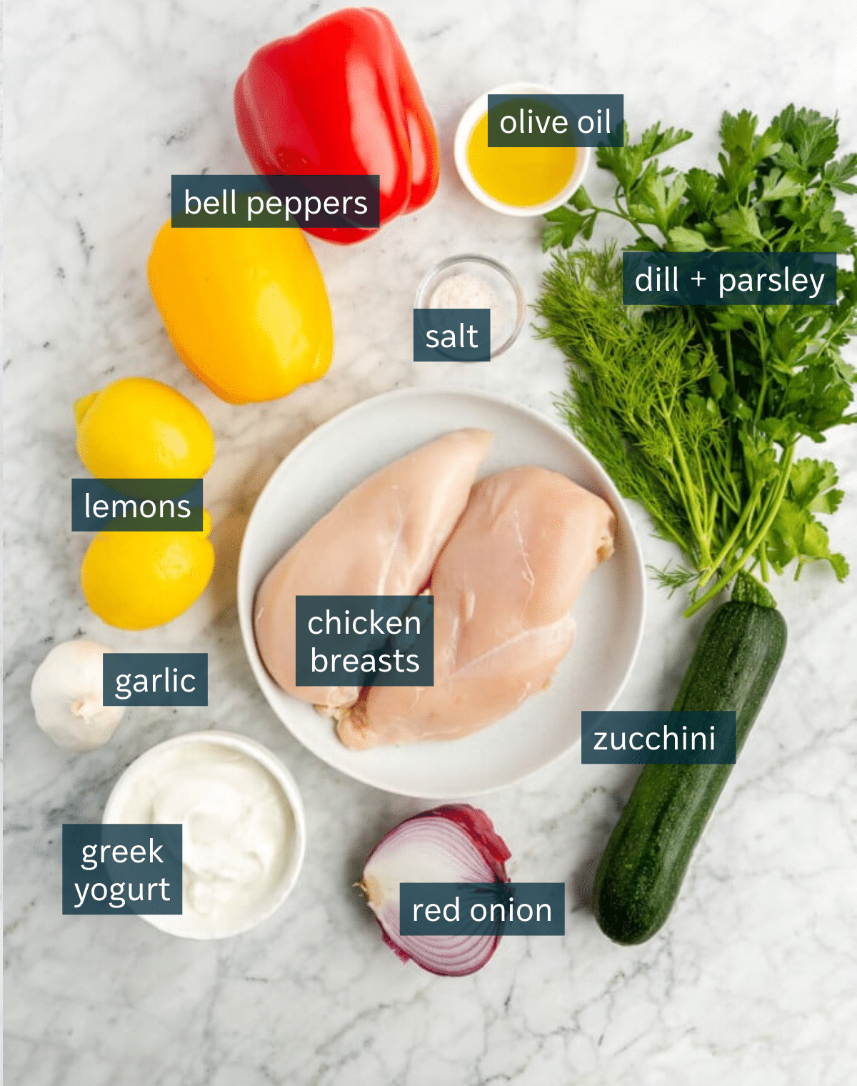 Ingredients for chicken kabobs with veggies sit on a marble countertop.