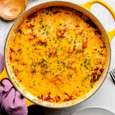 Fully prepared stuffed pepper casserole sits in the enameled yellow pot from which it was cooked. A wooden serving spoon and purple dishcloth sit to the side.