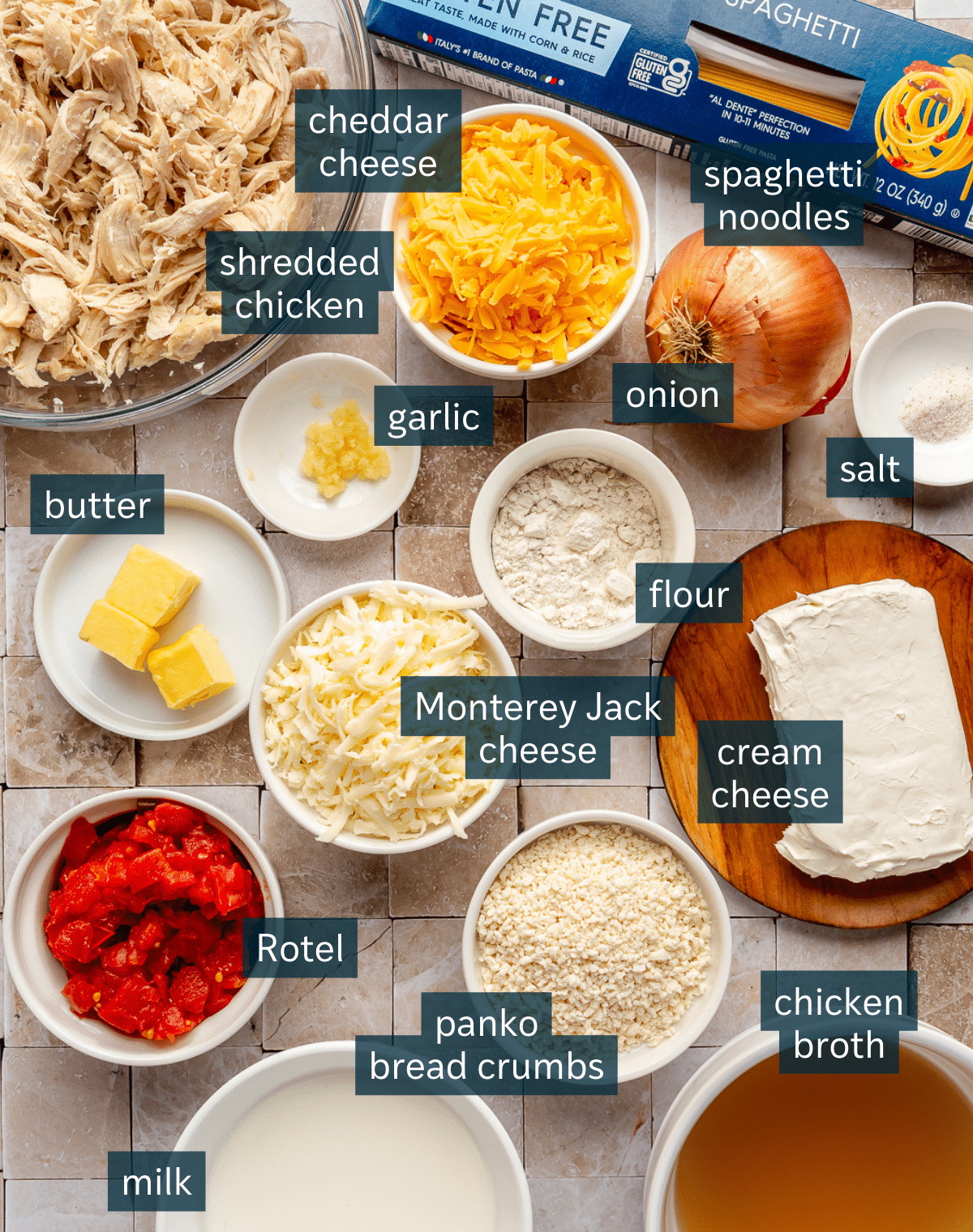 Ingredients for baked chicken spaghetti sit in a variety of bowls on a cream colored tile countertop.