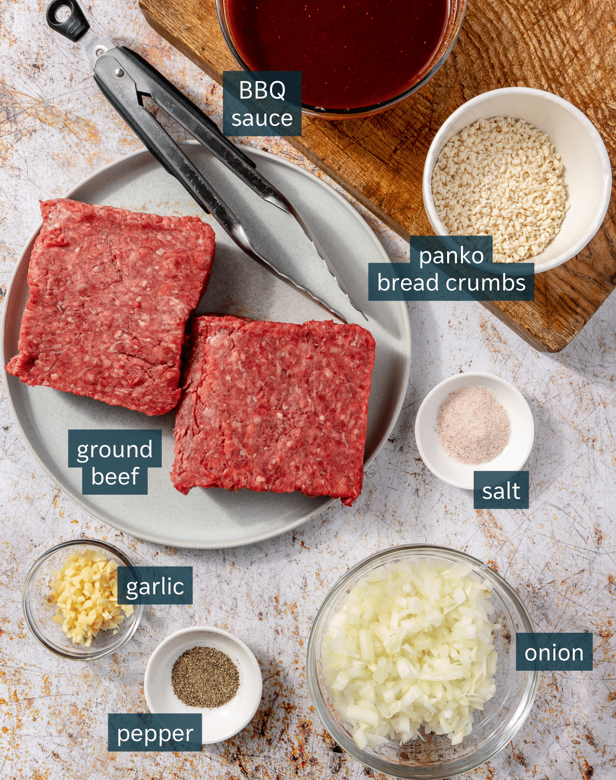 Ingredients for bbq meatballs sit in a variety of bowls and on a wooden chopping block.