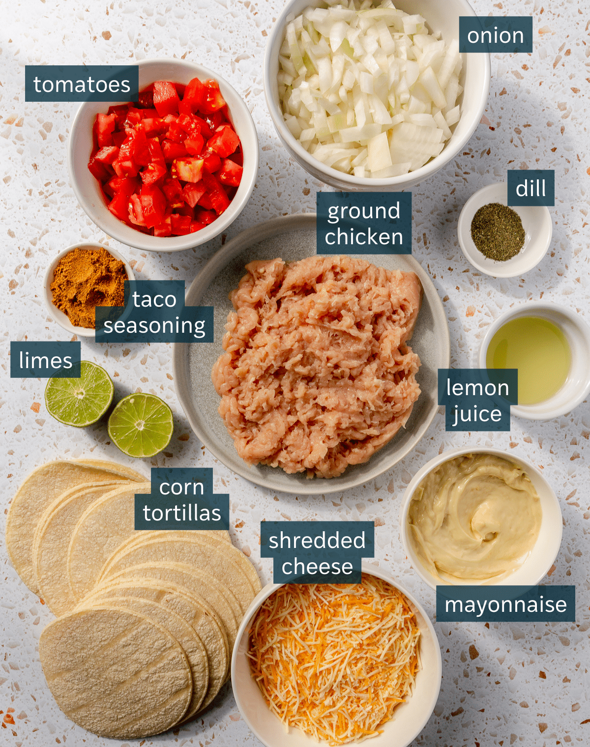 Ingredients for ground chicken tacos sit in a variety of bowls on a white speckled countertop.