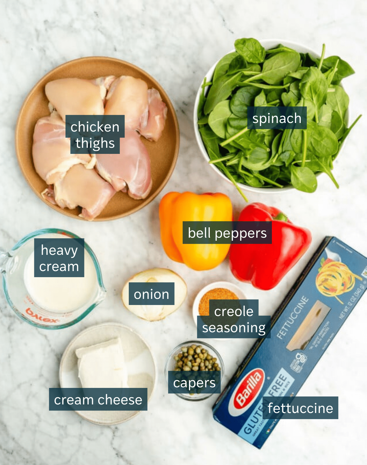 Ingredients for creamy cajun chicken pasta sit in a variety of bowls on a marble countertop.