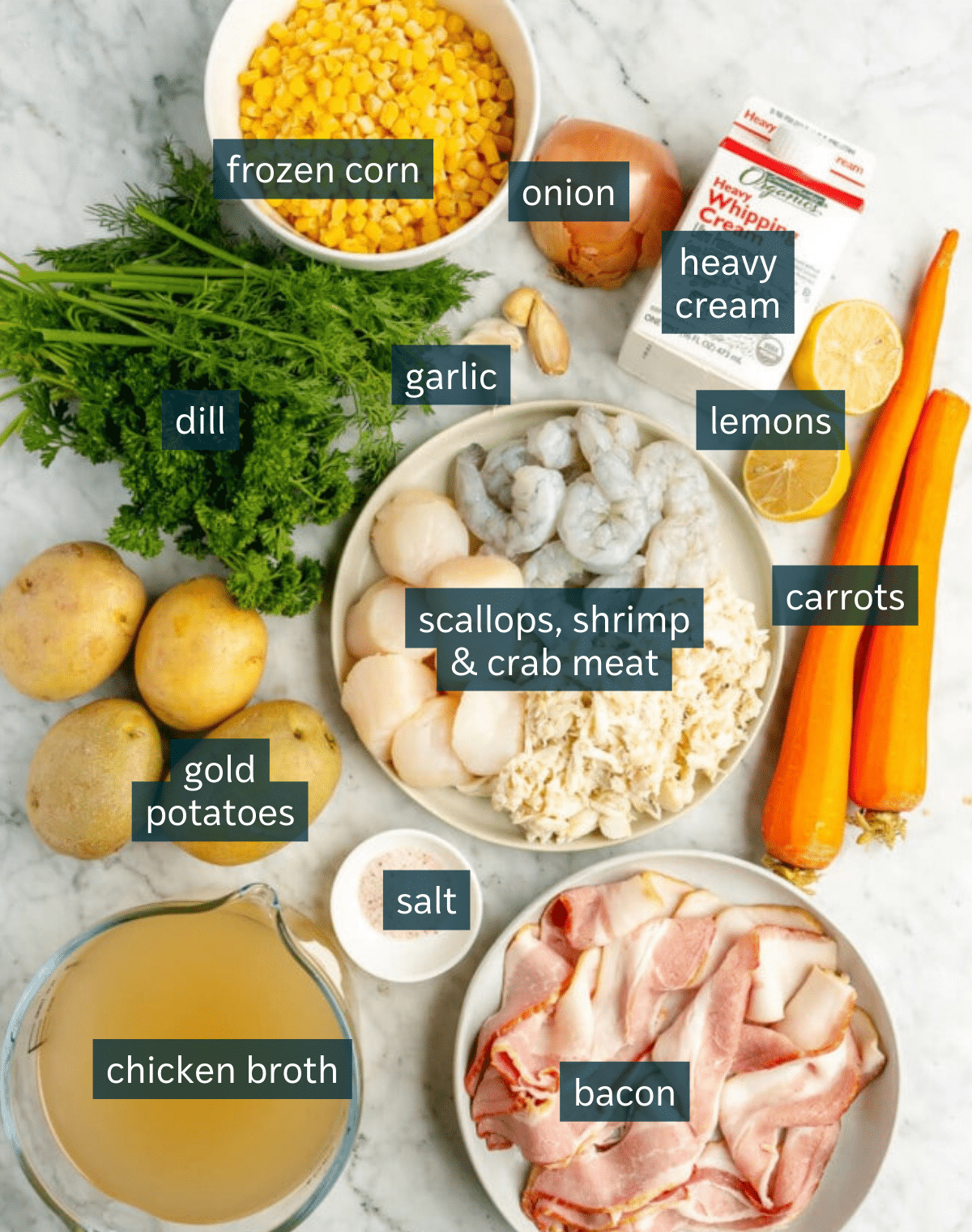 Ingredients for creamy seafood chowder sit in a variety of bowls on a marble countertop.