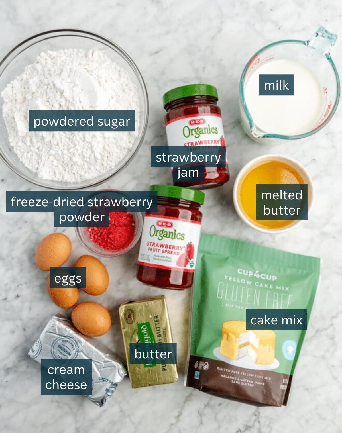 Ingredients for the best strawberry cake with cream cheese frosting sit in a variety of bowls on a marble countertop.