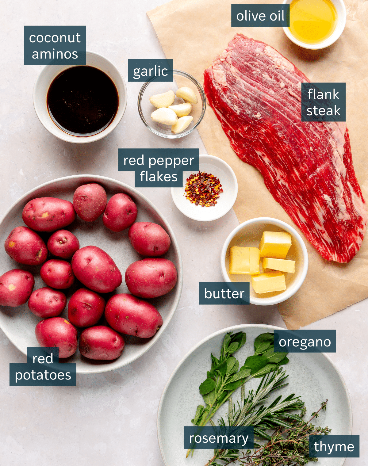 Ingredients for a garlic butter steak and potato skillet sit in a variety of bowls on a light colored surface.