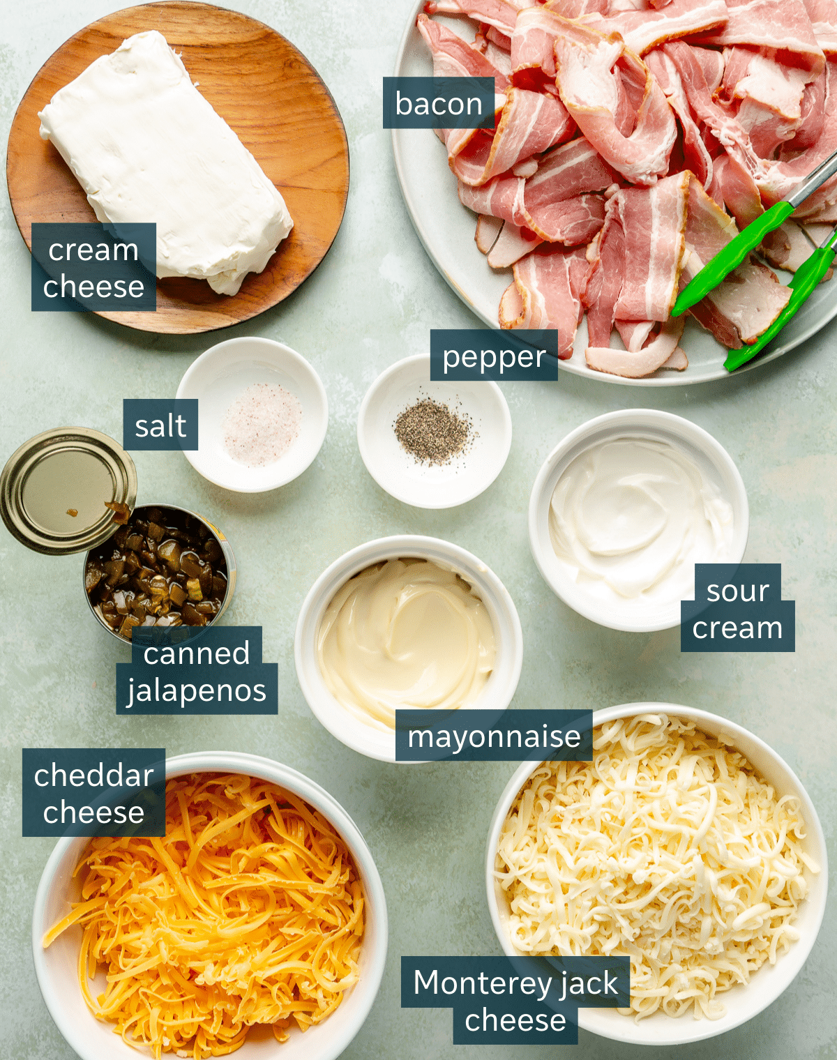 Ingredients for jalapeno popper dip sit in a variety of bowls on a light grey countertop.