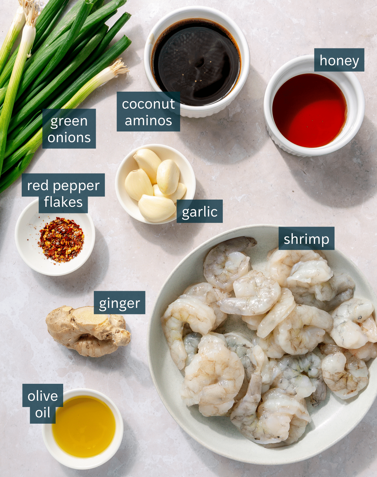 All of the ingredients needed for honey garlic shrimp in different sized bowls on a light pink surface.