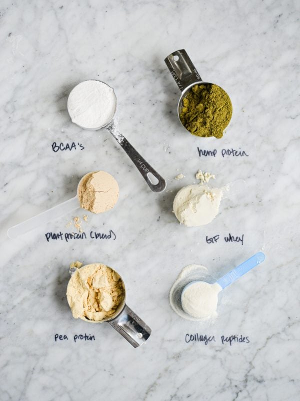 different protein powders in scoops or measuring cups with labels on a marble surface