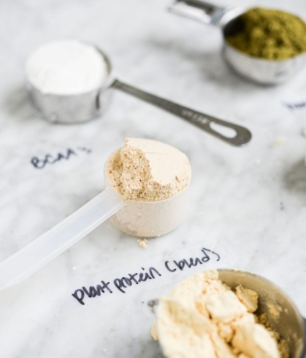 different protein powders in scoops or measuring cups with labels on a marble surface